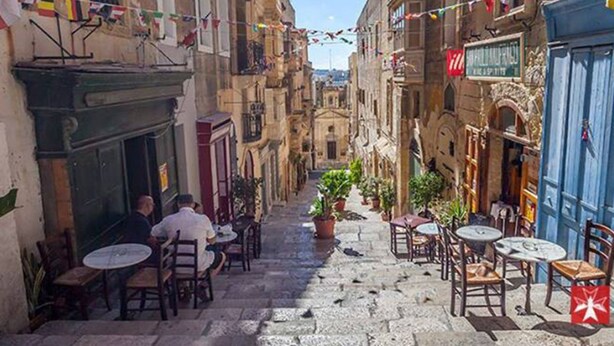 Una calle estrecha con mesas al aire libre y macetas con plantas.