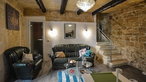 Ein gemütliches Wohnzimmer mit Steinwand, einer Ledersofa, einem Glastisch und einer Treppe, die in eine obere Ebene führt.