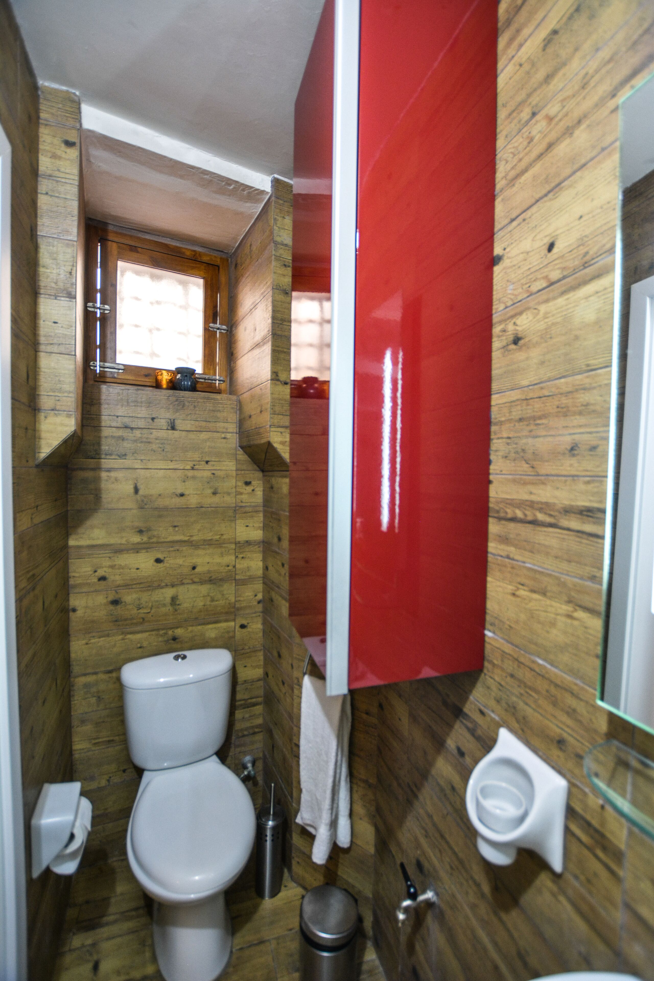 A compact bathroom with wooden walls, a white toilet, a bidet, and a small window.