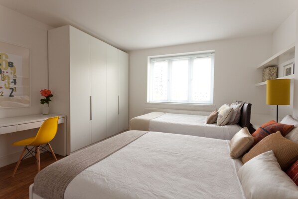 Un dormitorio con dos camas, un escritorio, una silla y una ventana.