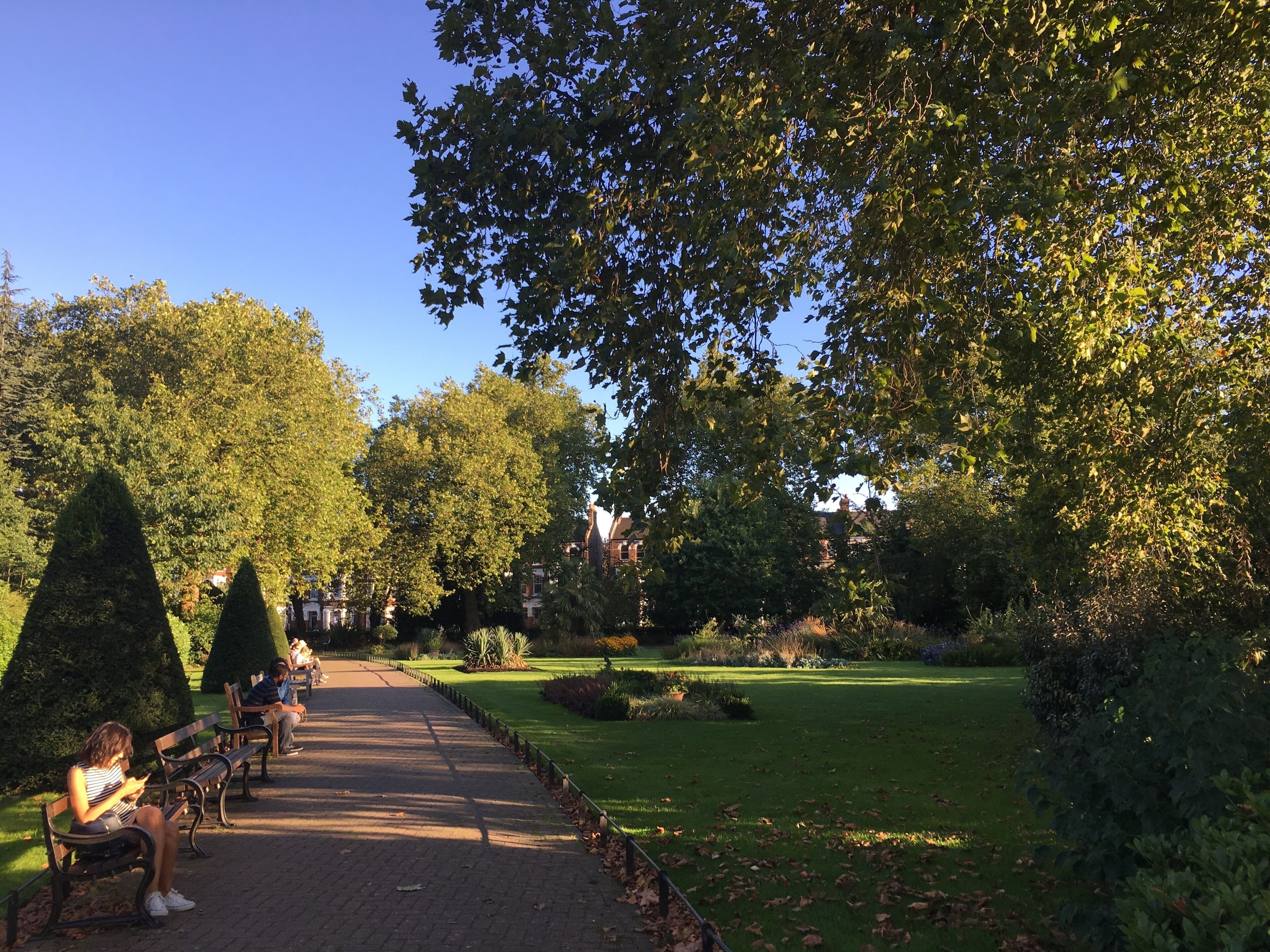 Un parc doté de bancs, d’une allée pavée et de pelouses bien entretenues.