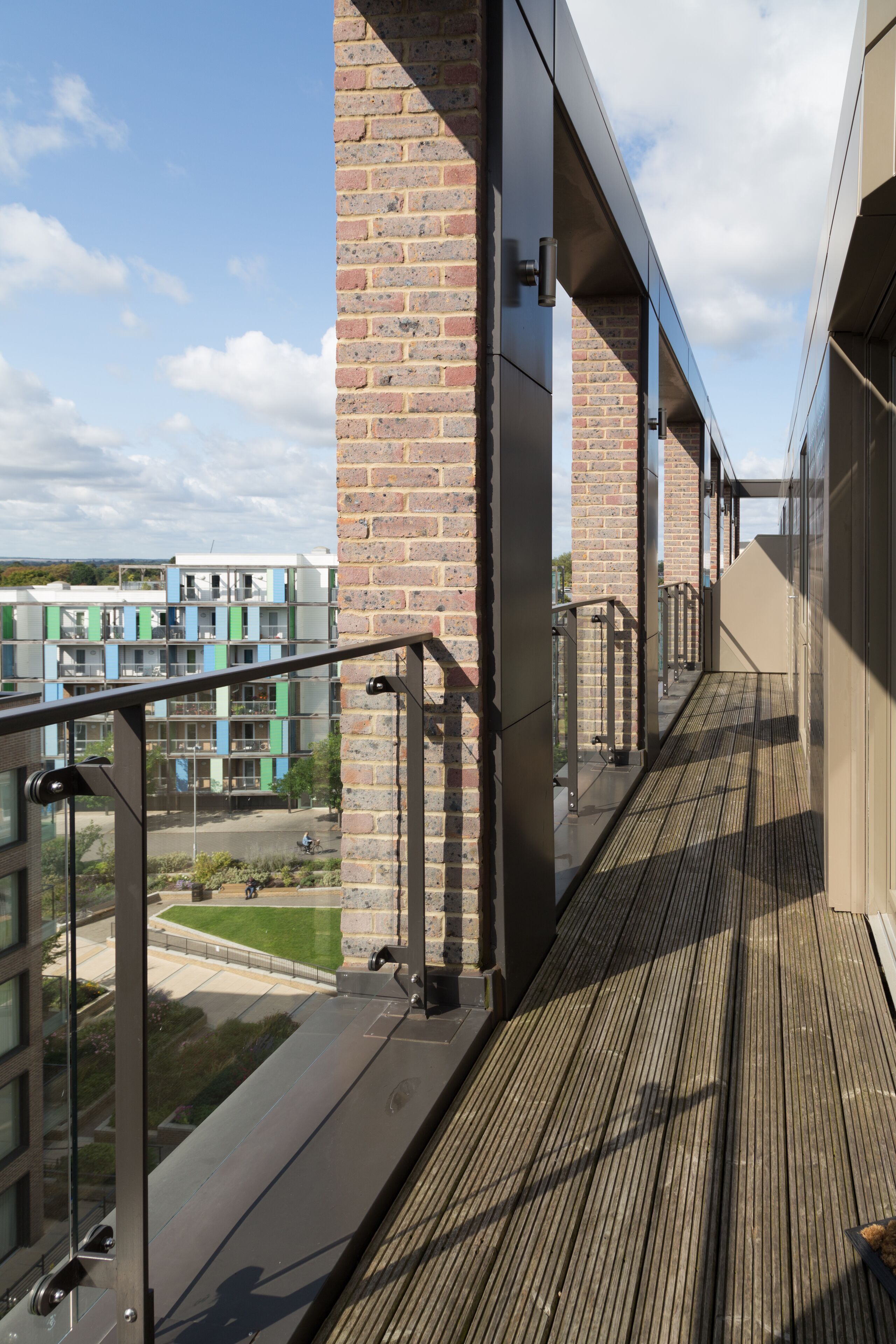 A modern building with a wooden deck, glass railings, and a brick wall.