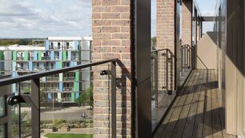 A modern building with a wooden deck, glass railings, and a brick wall.
