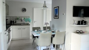 Een moderne keuken met witte kastjes, een eettafel met stoelen, een klok en een televisie op een plank.