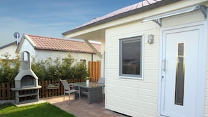Een terras met een barbecue, een tafel en stoelen.