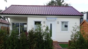 Een gelijkvloers huis met een rode dakbedekking, witte gevel en een voordeur met een klein portaaltje.