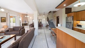 En rummelig opholdsstue med sofa, spisebord og et køkkenområde med køleskab og mikroovn.