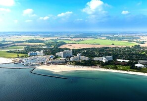 An aerial view of a coastal area with a marina, buildings, and green fields.