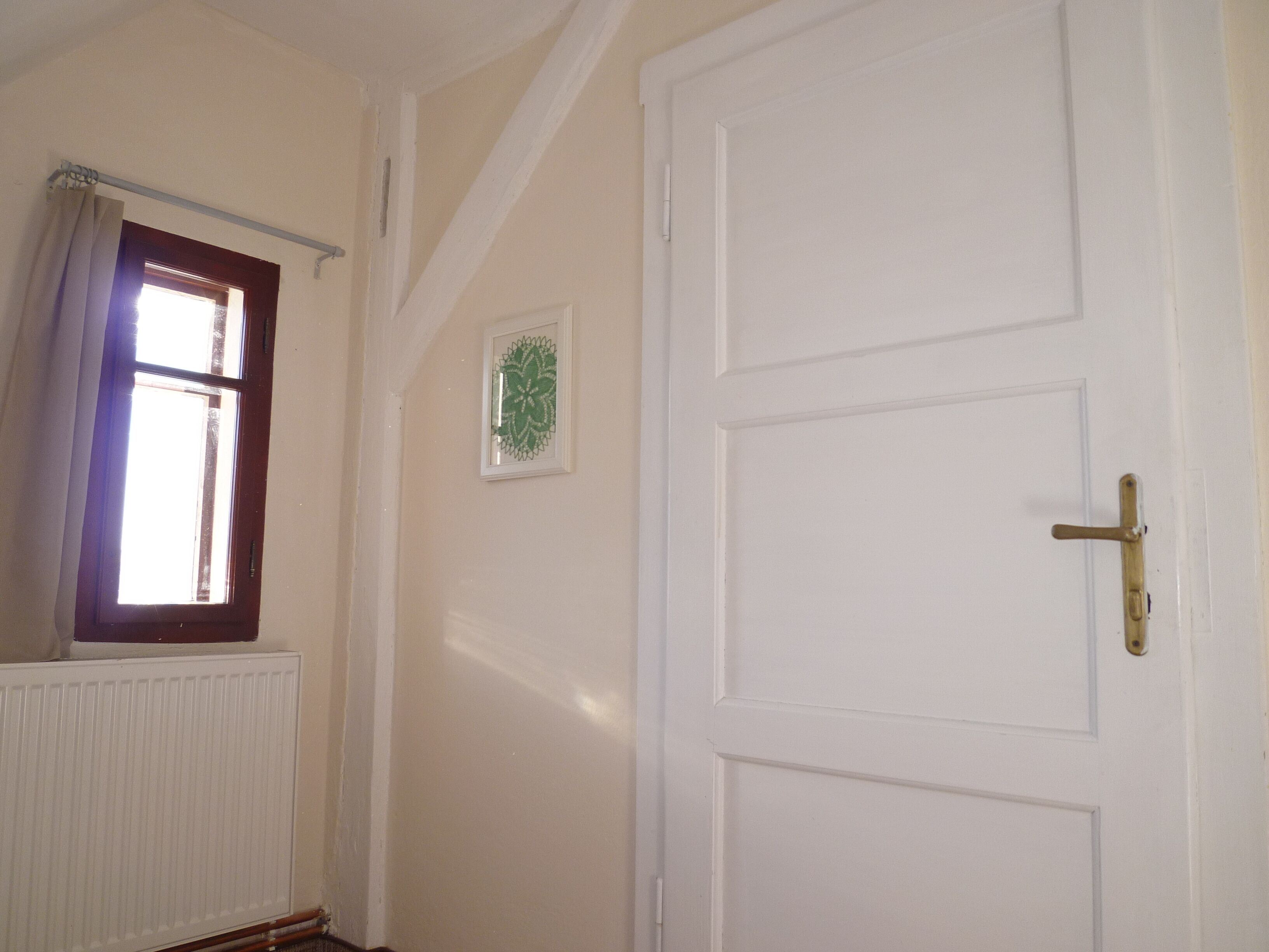 Een kamer met een witte deur, een raam met gordijn en een radiator.