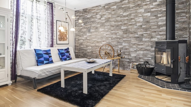 Uma sala de estar moderna com um sofá branco, tapete preto e uma lareira com parede de pedra ao fundo.