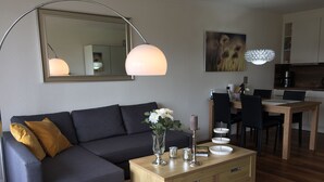 A modern living room with a dark grey sectional sofa, a wooden coffee table, a mirror, and a dining area with a wooden table and chairs. - Romantic apartment with fantastic views, WiFi free (Winterberg)