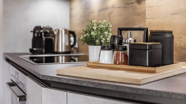 A modern kitchen with a wooden countertop, a coffee machine, a kettle, and a potted plant.