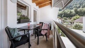 A balcony with wicker chairs, a table, and a potted plant.