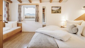 A bedroom with a wooden ceiling, a bed with white bedding, a window with curtains, and a painting on the wall.