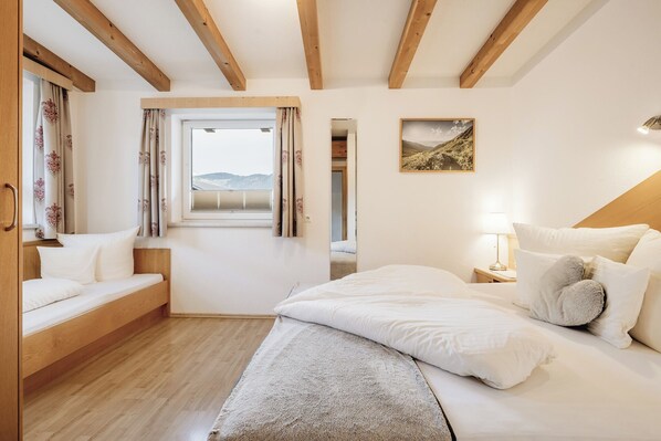 Un dormitorio con techo de madera, una cama con ropa de cama blanca, una ventana con cortinas y un cuadro en la pared.