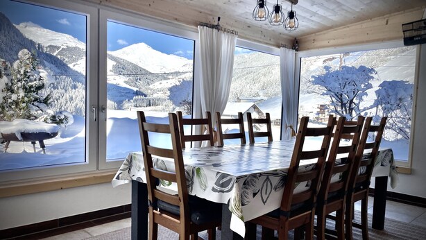 A dining area with a table and chairs, large windows with a snowy mountain view, and wooden ceiling beams. - Holiday apartment for up to 8 people! No dogs! (Tux)