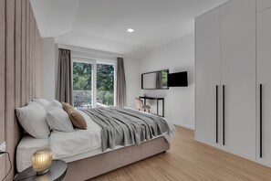 Une chambre moderne comprenant un lit, une table de chevet, une télévision, une armoire et une fenêtre avec des rideaux.