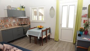Eine kompakte Küche mit Esstisch für zwei Personen, einer kleinen Couch und einem Fenster mit Vorhängen.