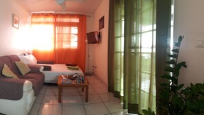 A living room with a sofa, a coffee table, and a television on the wall. - Manava Tahara'a home stay (Mahina)