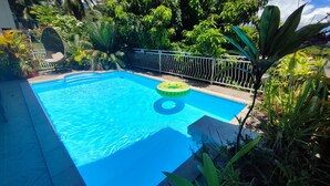 A clear blue swimming pool with a floating ring, surrounded by lush greenery and a metal fence. - Manava Tahara'a home stay (Mahina)