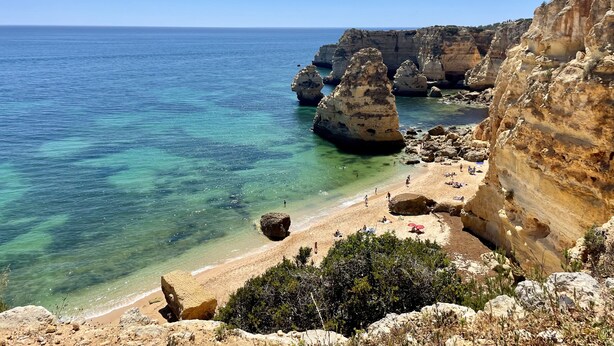 Una playa costera con aguas turquesas cristalinas, acantilados rocosos y una orilla arenosa.