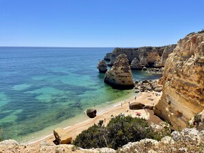 Una playa costera con aguas turquesas cristalinas, acantilados rocosos y una orilla arenosa.