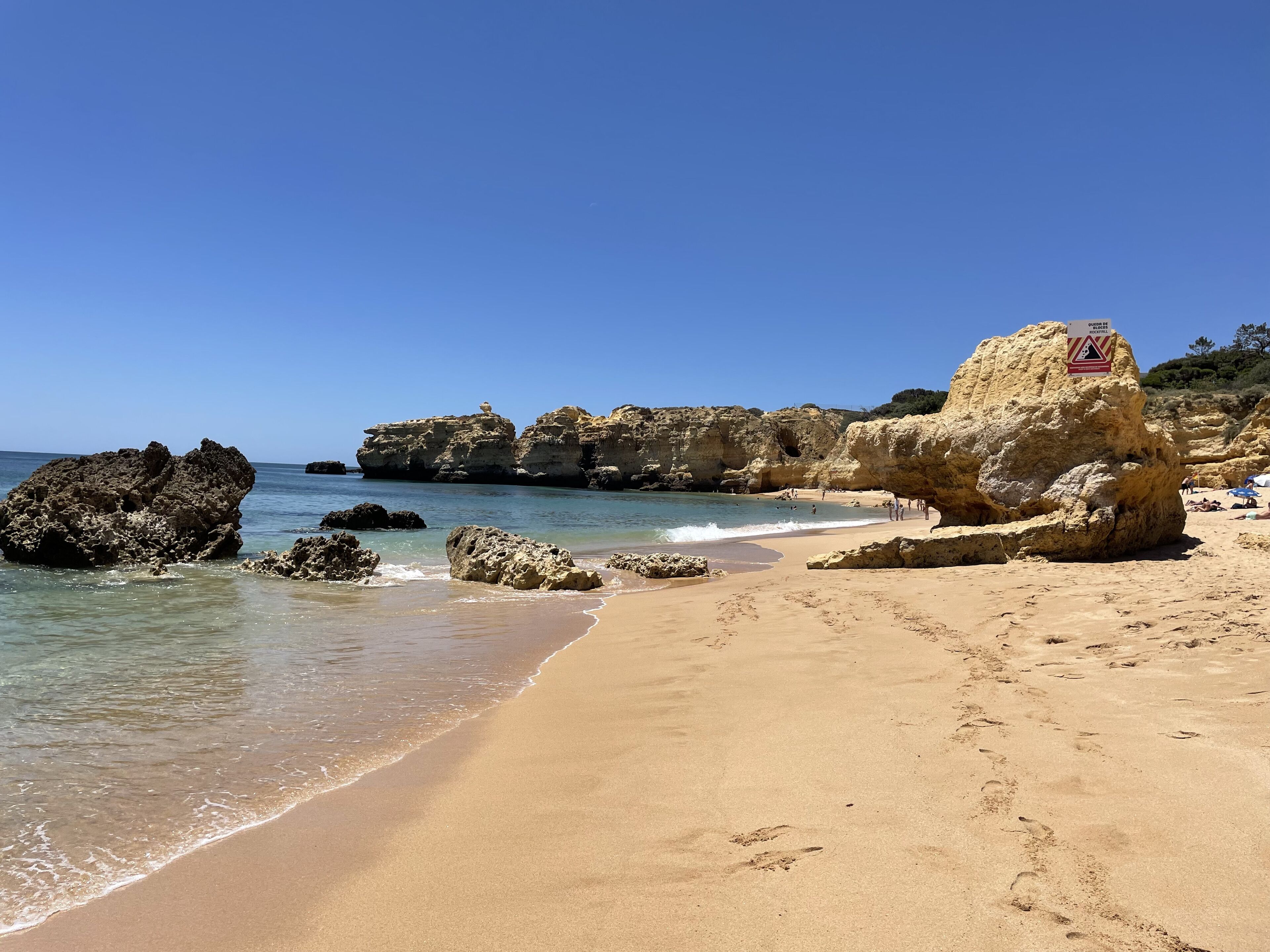 A beach with clear blue water, rocky formations, and a warning sign.