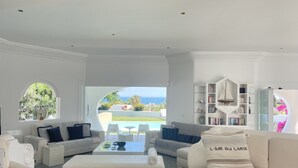 Amplia sala de estar con vista al océano, una piscina y una estantería.