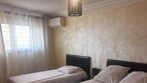 Une chambre avec deux lits, un luminaire suspendu, un appareil de climatisation et une fenêtre avec des rideaux.
