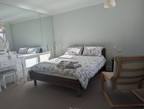 Une chambre à coucher avec un lit, une table de chevet, une chaise, un miroir et une fenêtre.
