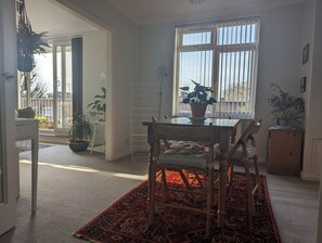 Une pièce comprenant une table à manger, des chaises, un tapis rouge à motifs, une fenêtre avec des barreaux et plusieurs plantes en pot.