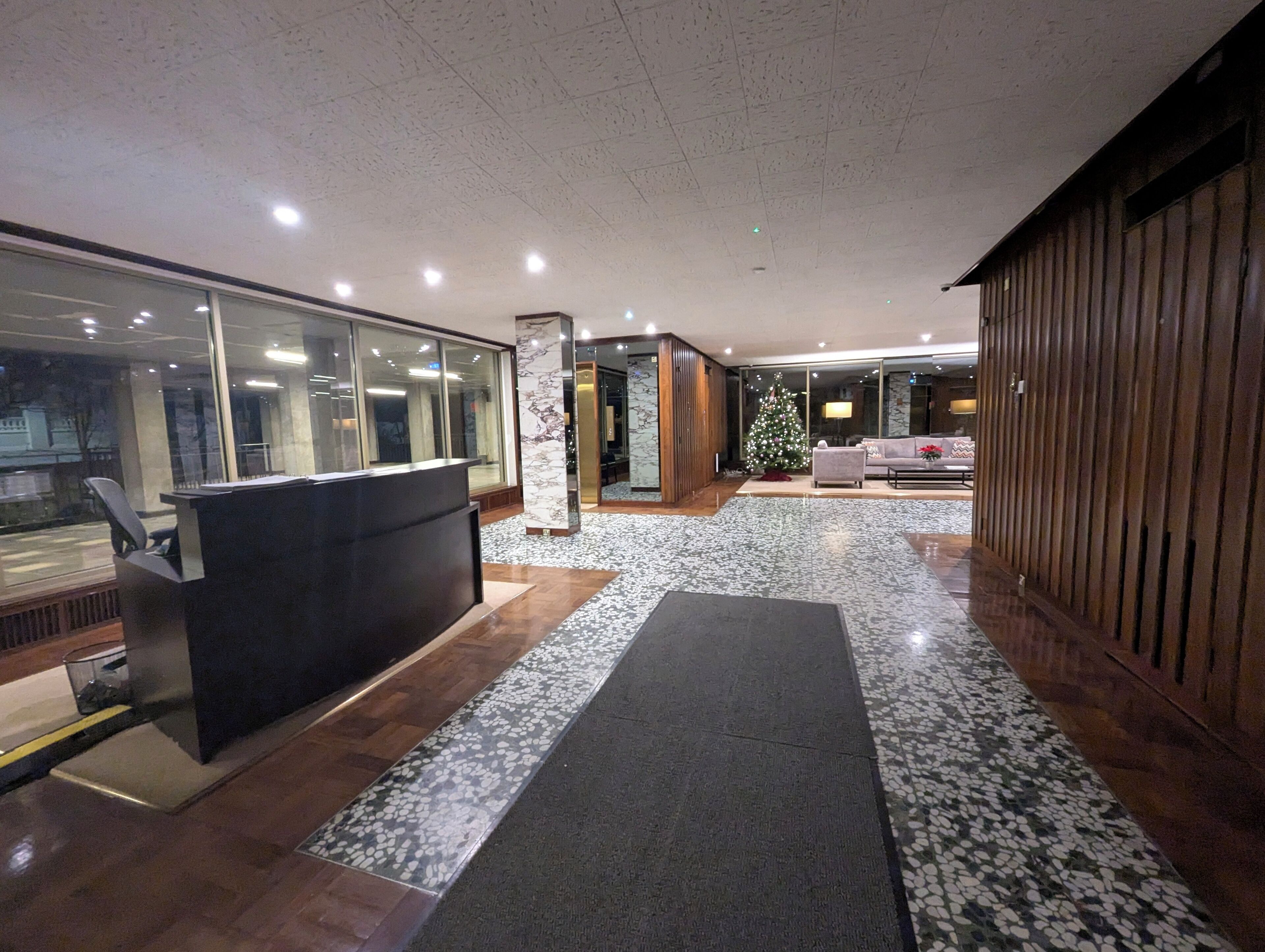 Eine moderne Lobby mit einer Rezeption, einem Weihnachtsbaum und einer Sitzecke mit einer Couch und Sesseln.