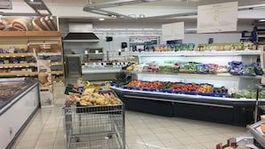 A grocery store interior with a refrigerated section, produce display, and a shopping cart.
