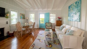 A spacious living room with a fireplace, white furniture, and a large window with a blue door. - Beachy Perfection - Walk to Atlantic Ave. (Delray Beach)
