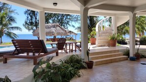 A covered outdoor area with a pool, lounge chairs, and potted plants. -  Beachfront Private Pool Home  -  A "Gold Standard Facility" (Placencia)