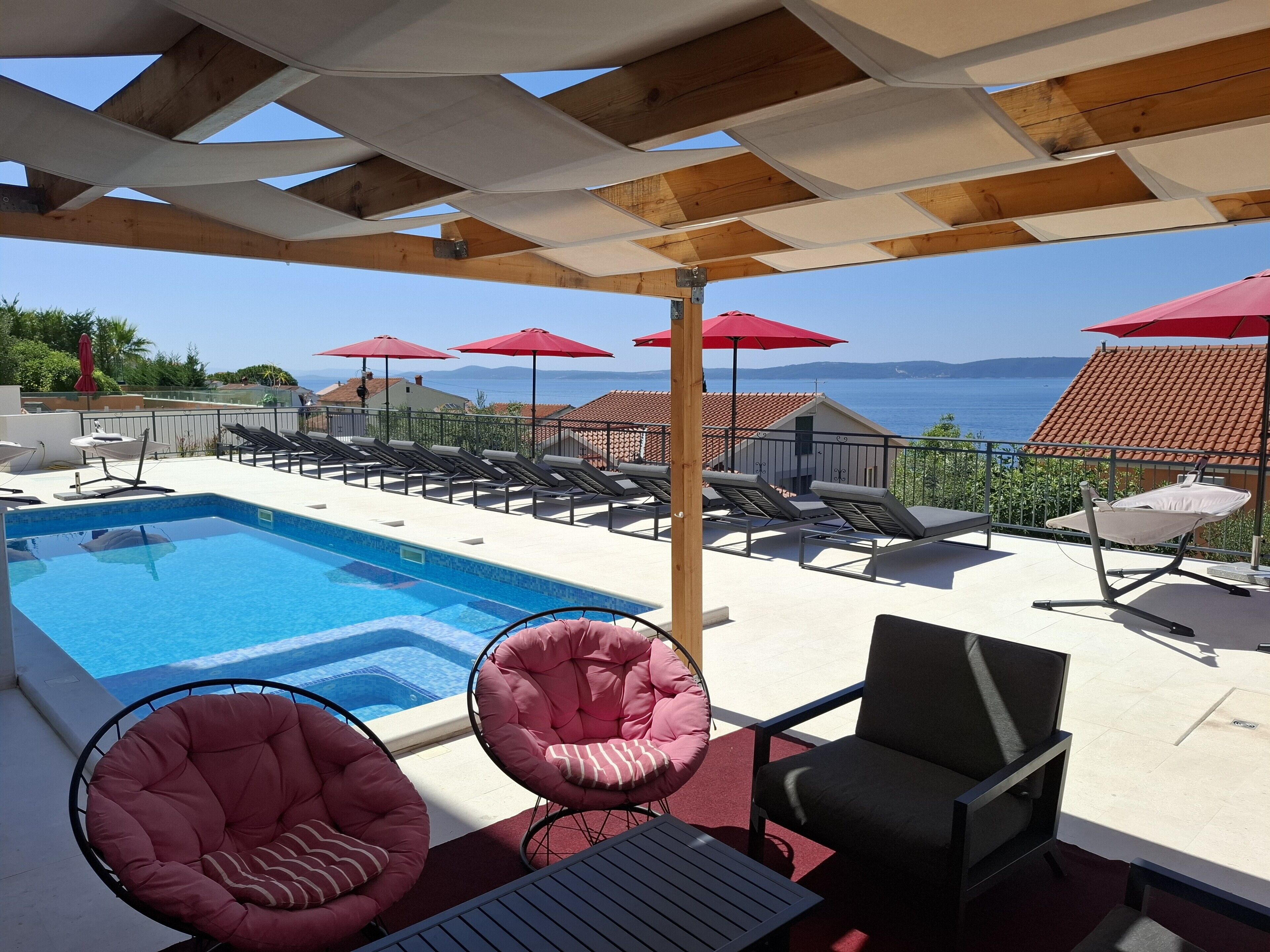 Ett område vid poolen med fri utsikt över havet, solstolar och parasoller.