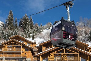 Un télésiège avec des cabines, des bâtiments en bois et, au loin, des arbres recouverts de neige.