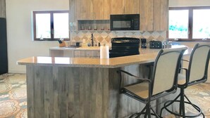 A modern kitchen with wooden cabinets, a central island with bar stools, a microwave, and a stove.