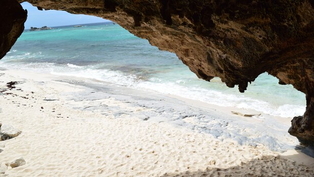 A beach with clear turquoise water, white sand, and a rocky cave formation.