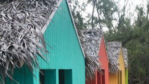 A row of colorful beach huts with thatched roofs, lined up along a sandy path.