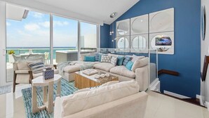 A modern living room with a large window overlooking the ocean, a beige sofa set, a coffee table, and a blue accent wall. - Heaven can wait,I found a paradise with Ocean view (Noord)