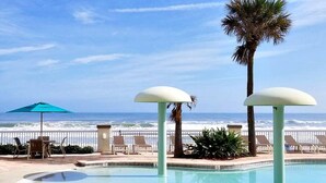 A pool area with lounge chairs and umbrellas, overlooking the ocean. - Ocean Views | Pool | 8th Floor 1BR | Sleeps 6 | Free Daily Activities (Daytona Beach)