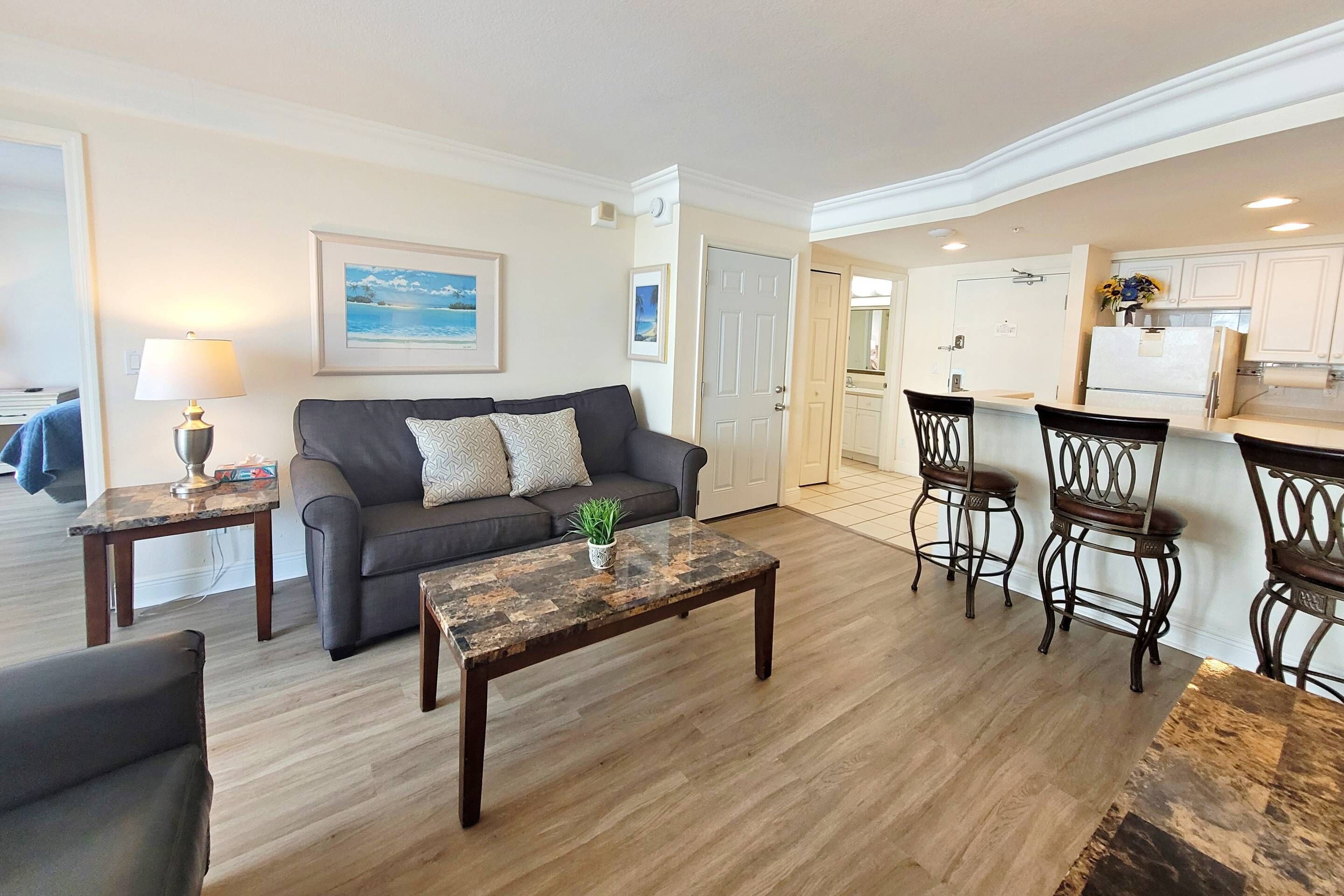 A living room with a sofa, coffee table, and a dining area with chairs and a kitchen in the background.