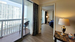 A hotel room with a balcony, a desk with a lamp, and a bed with a blue cover. - Ocean Views | Pool | 8th Floor 1BR | Sleeps 6 | Free Daily Activities (Daytona Beach)