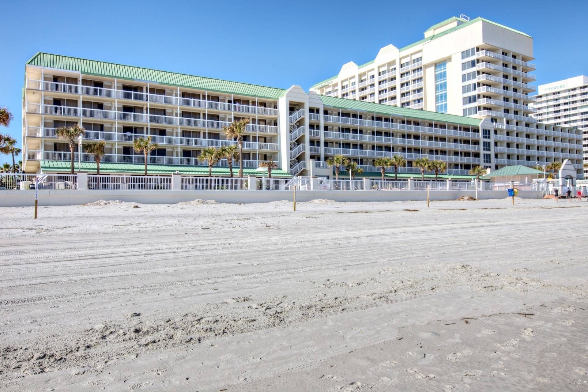 A multi-story hotel with balconies, located near a sandy beach.