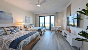 A hotel room with two beds, a balcony, a TV, and a dining area. - Beachfront Studio | Ground-Floor Patio + Ocean Views | Steps to Sand | Free Activities Included (Daytona Beach Shores)