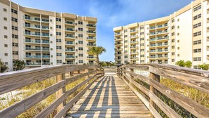 Un paseo marítimo de madera que lleva a un edificio residencial de varios pisos con balcones.