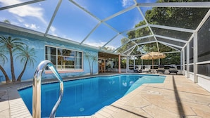 A swimming pool with a glass enclosure, a patio area with lounge chairs, and a view of the surrounding landscape. - Specials - 3BR with Pool, Walk to Town (Cape Coral)