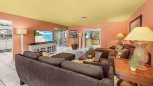 A living room with a sofa, coffee table, and lamps. There is a television and a plant on the coffee table. - Specials - 3BR with Pool, Walk to Town (Cape Coral)