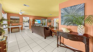 A spacious living area with a ceiling fan, a large painting, and a dining table. - Specials - 3BR with Pool, Walk to Town (Cape Coral)